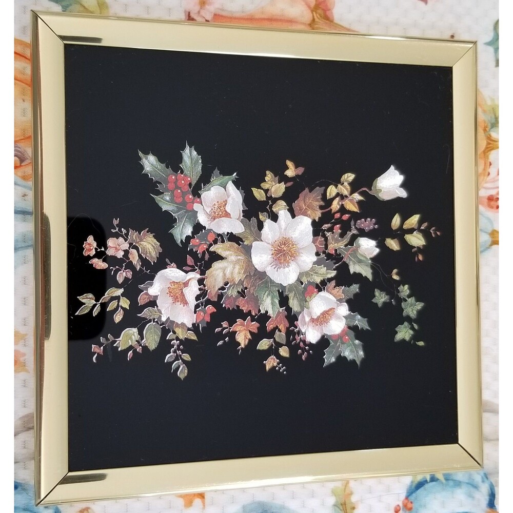Silk flowers on black background with gold tone frame.